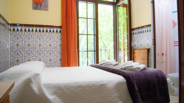 Une chambre d’hôtel avec un grand lit, une fenêtre avec des rideaux orange et des murs recouverts de carreaux à motifs.