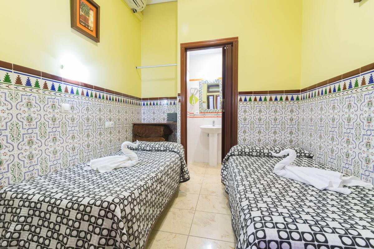 Habitación de hotel con dos camas, cada una con una toalla doblada en forma de cisne, un lavamanos y un espejo.