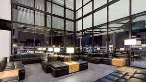 A modern lounge area with leather sofas, wooden tables, and large windows offering views of the cityscape. - Ramada Encore by Wyndham San Luis Potosi (San Luis Potosi)