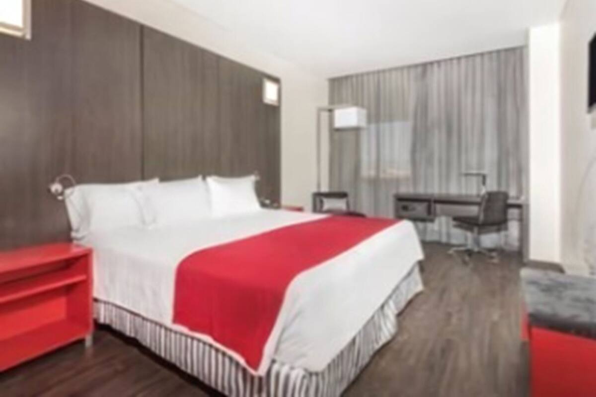A hotel room with a bed, a desk, a chair, and a TV.