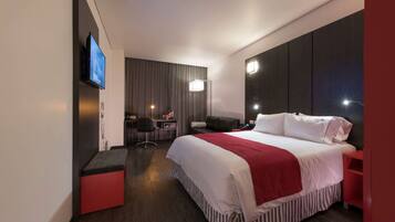 A modern hotel room with a large bed, a desk, a chair, and a TV mounted on the wall.