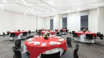 A conference room with multiple round tables, each covered with a red tablecloth and surrounded by black chairs.