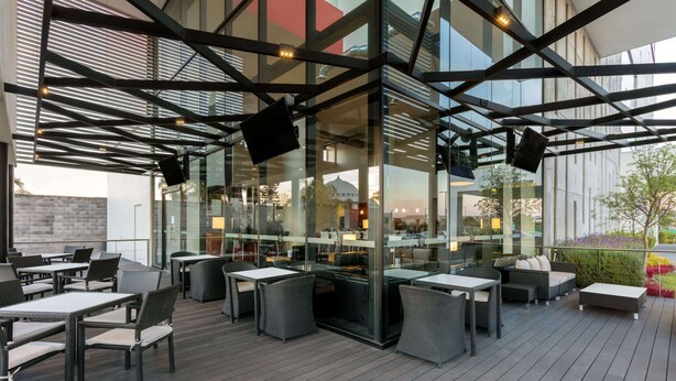 An outdoor seating area with tables and chairs, a glass enclosure, and a view of the surrounding area. - Ramada Encore by Wyndham San Luis Potosi (San Luis Potosi)