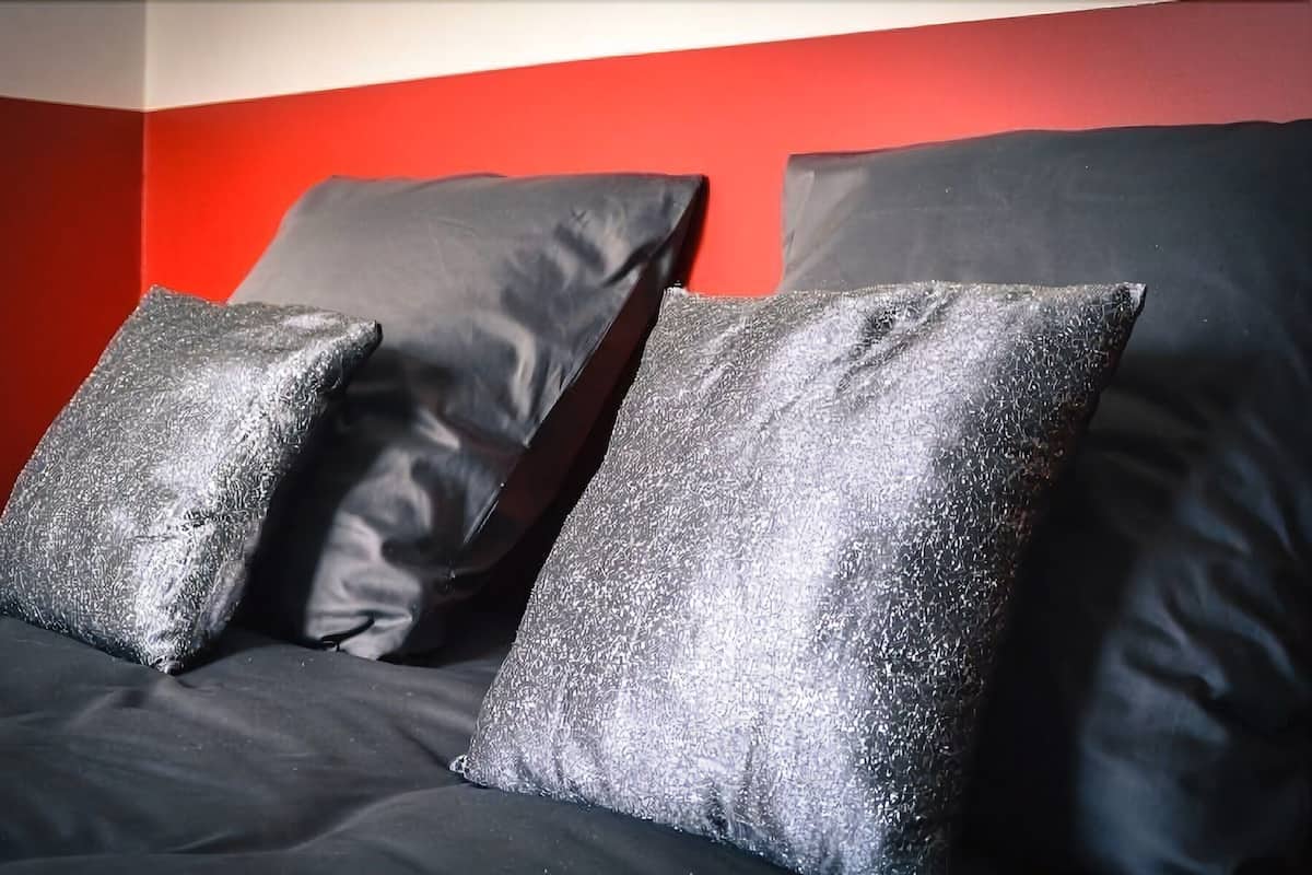 A bed with black bedding and silver-textured pillows against a red wall.