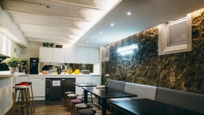 A modern kitchen with white cabinets, a black countertop, and a stone accent wall. There is a dining area with a black table and wooden stools. - Beautiful Belleville Hostel & Hotel (Paris)