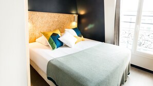 A neatly made bed with a patterned bedspread and pillows in various colors. - Beautiful Belleville Hostel & Hotel (Paris)