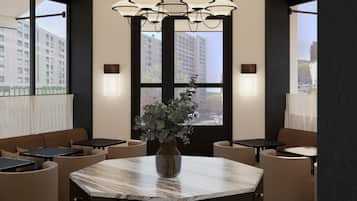 A modern dining area with a marble table, cushioned seating, pendant lighting, and large windows offering city views.