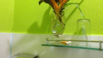 A bathroom with a green wall, a glass shelf holding a vase with a plant, and a toilet paper holder.