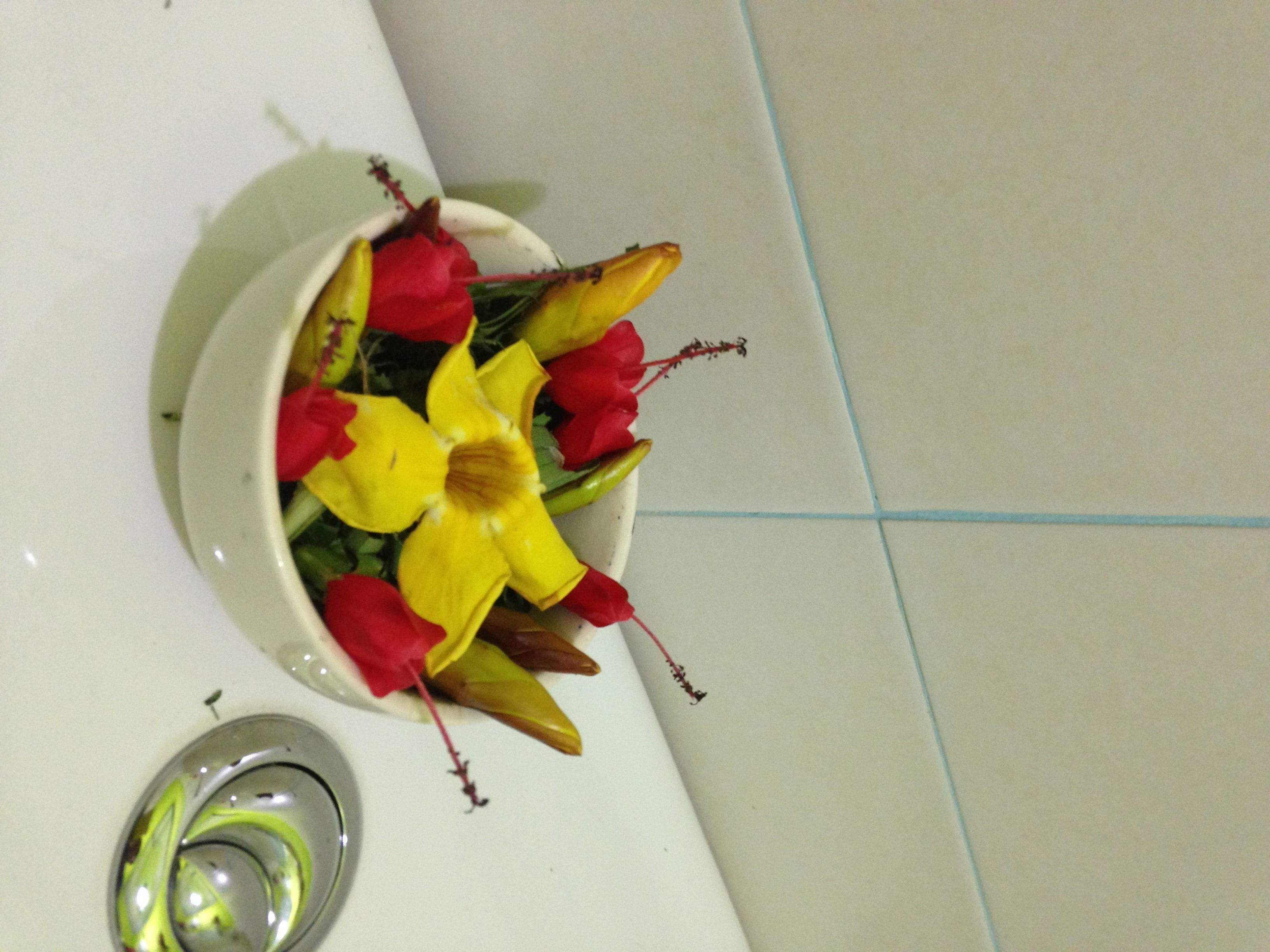 Un tazón de cerámica blanca con flores amarillas y rojas sobre una superficie de baldosas blancas.