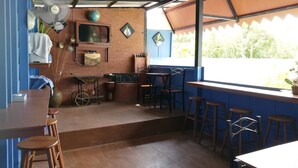 A rustic cafe with a brick wall, wooden stools, a small bar area, and a large window with a view of greenery. - The Box Chalet (Langkawi)