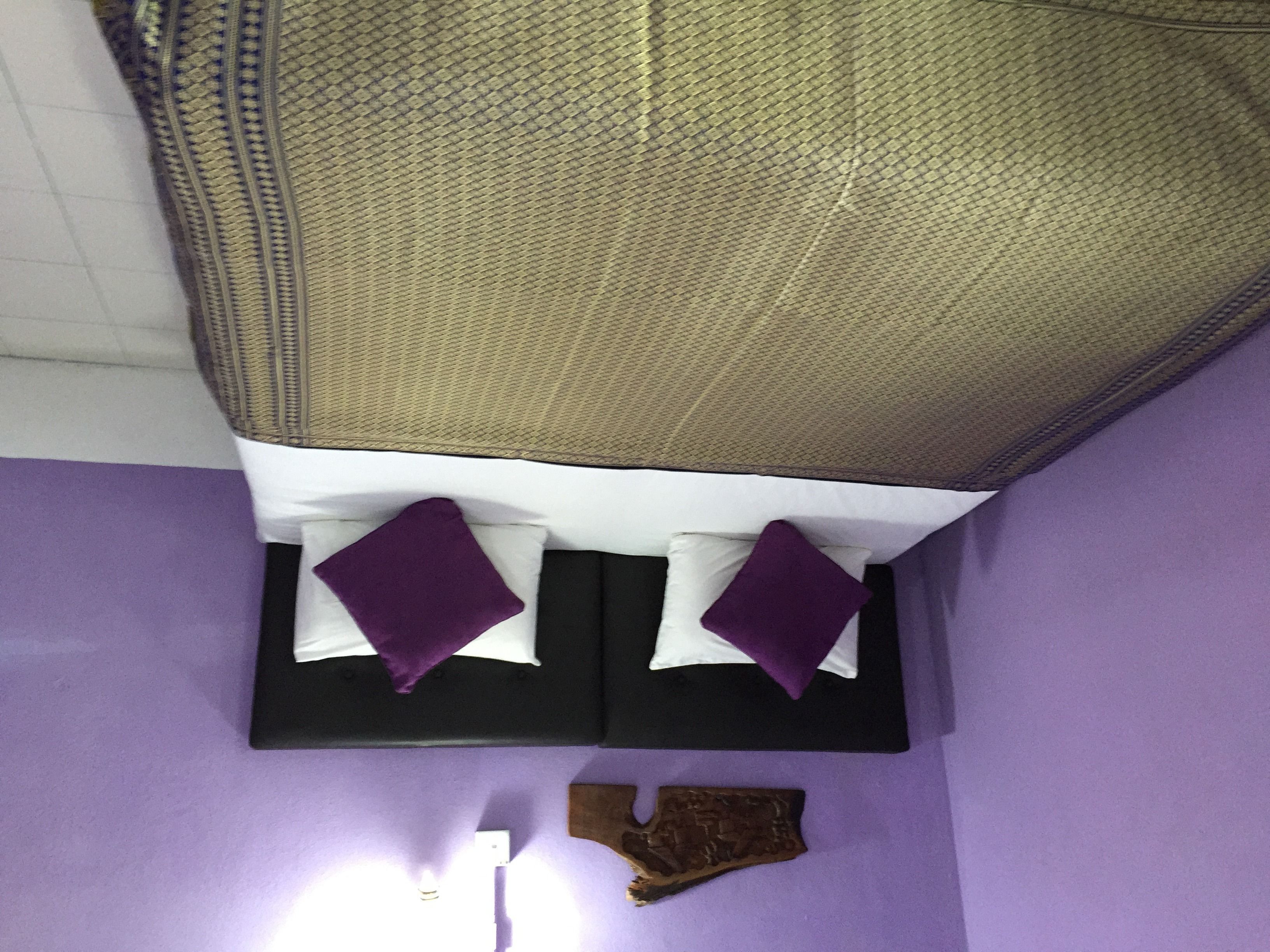 A room with a bed, two pillows, a wall-mounted light, and a wooden object on the floor.