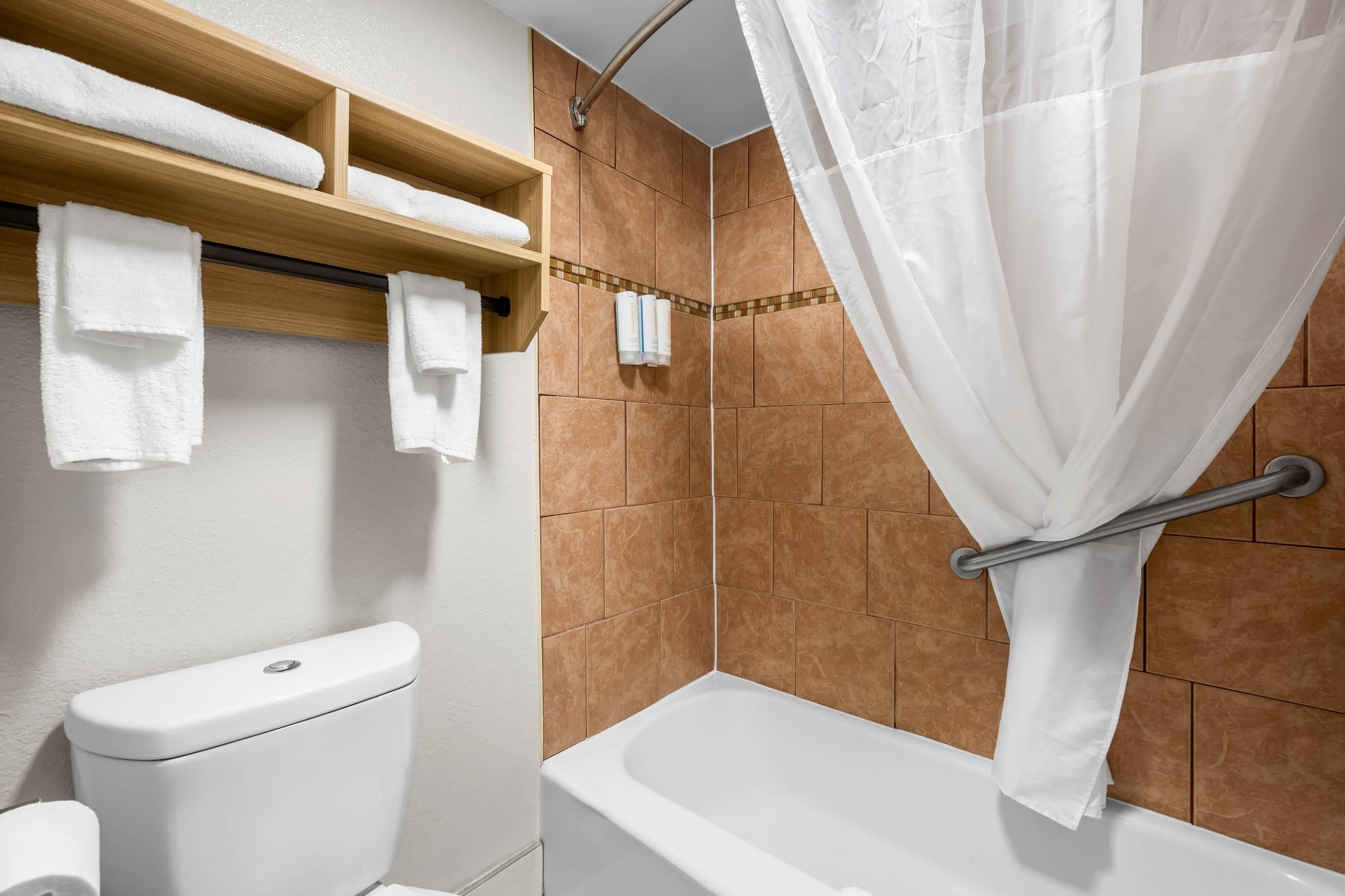 A bathroom with a toilet, a shower with a glass door, and a shelf with towels.