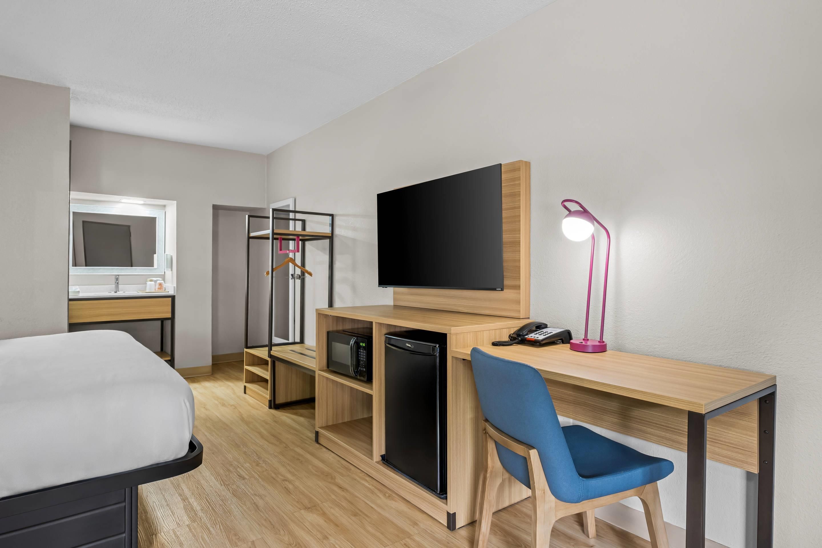 Une chambre d’hôtel comprenant un lit, un bureau avec un ordinateur, une télévision, une lampe de bureau et une chaise.