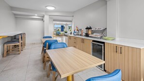 A modern kitchen with wooden cabinets, a built-in dishwasher, and a dining area with blue chairs and a wooden table. - Park Inn by Radisson, Weldon - Roanoke Rapids (Weldon)