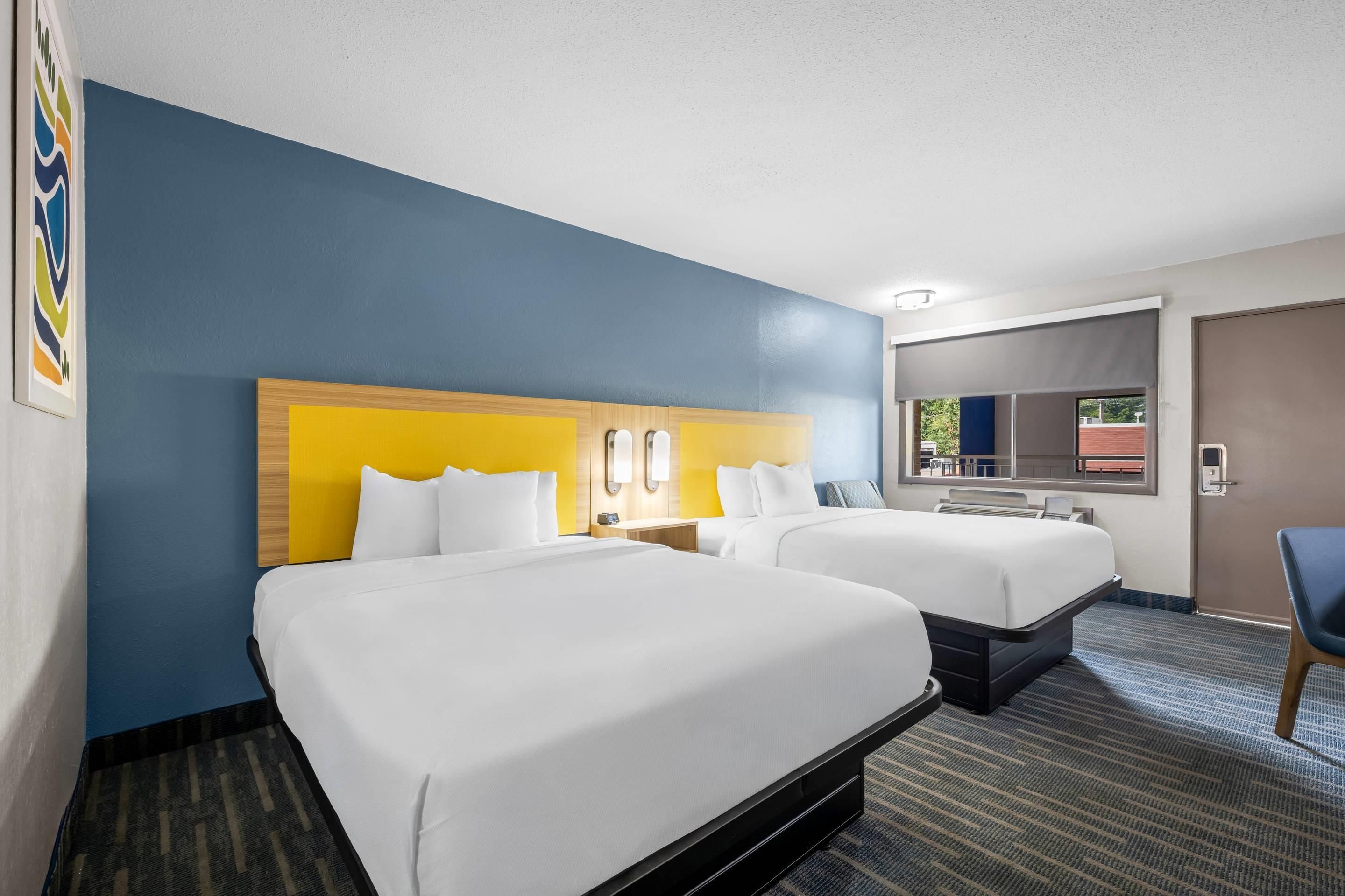 A hotel room with two beds, a large mirror, and a window with a view.