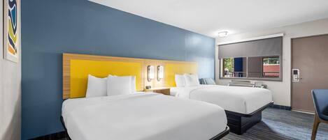 A hotel room with two beds, a large mirror, and a window with a view.