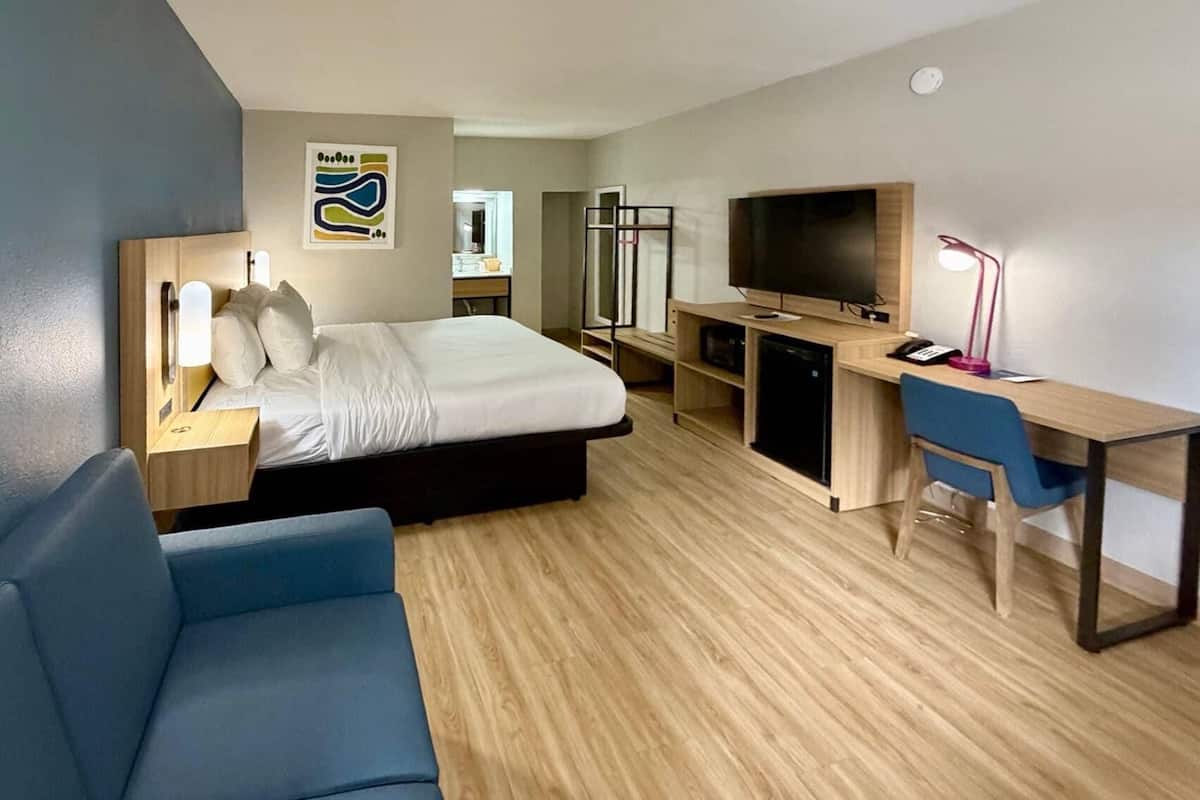Una habitación de hotel con cama, escritorio, computadora, televisor, silla y lámpara de escritorio.