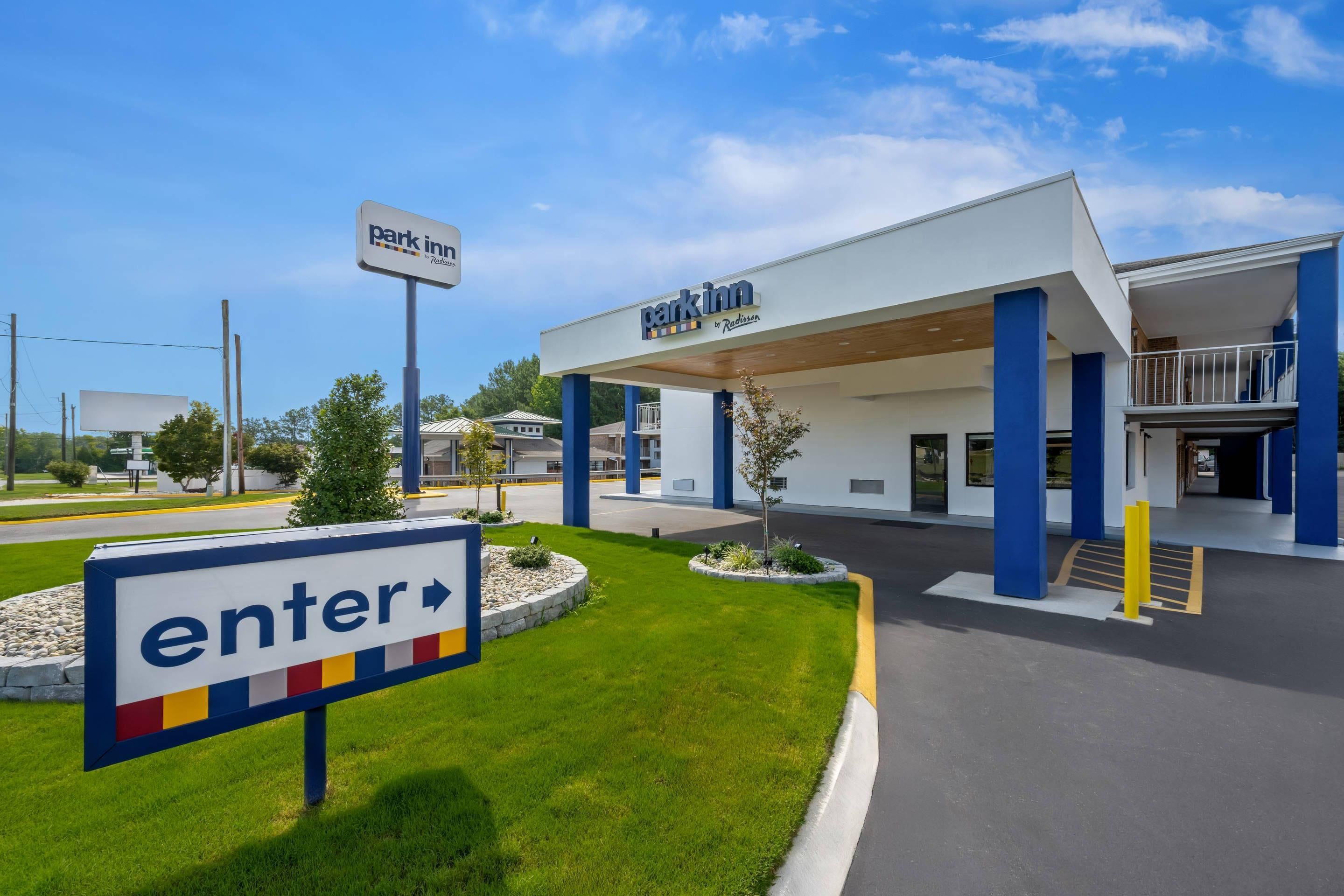 A park inn with a clear entrance sign, a gas station, and a well-maintained lawn area.