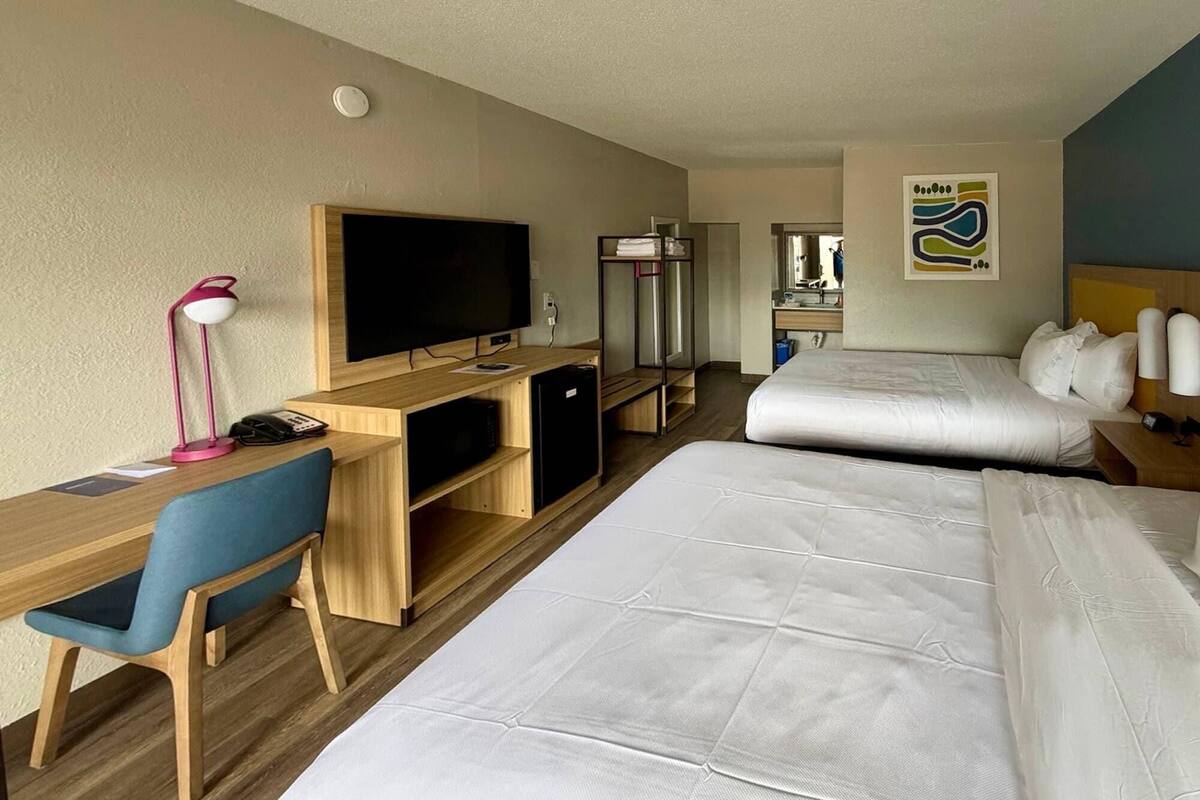 Una habitación de hotel con escritorio, televisión, cama y un baño visible al fondo.