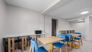 A modern dining area with multiple tables and chairs, a microwave, and a whiteboard on the wall.