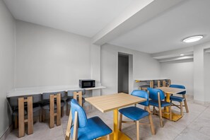 A modern dining area with multiple tables and chairs, a microwave, and a whiteboard on the wall. - Park Inn by Radisson, Weldon - Roanoke Rapids (Weldon)