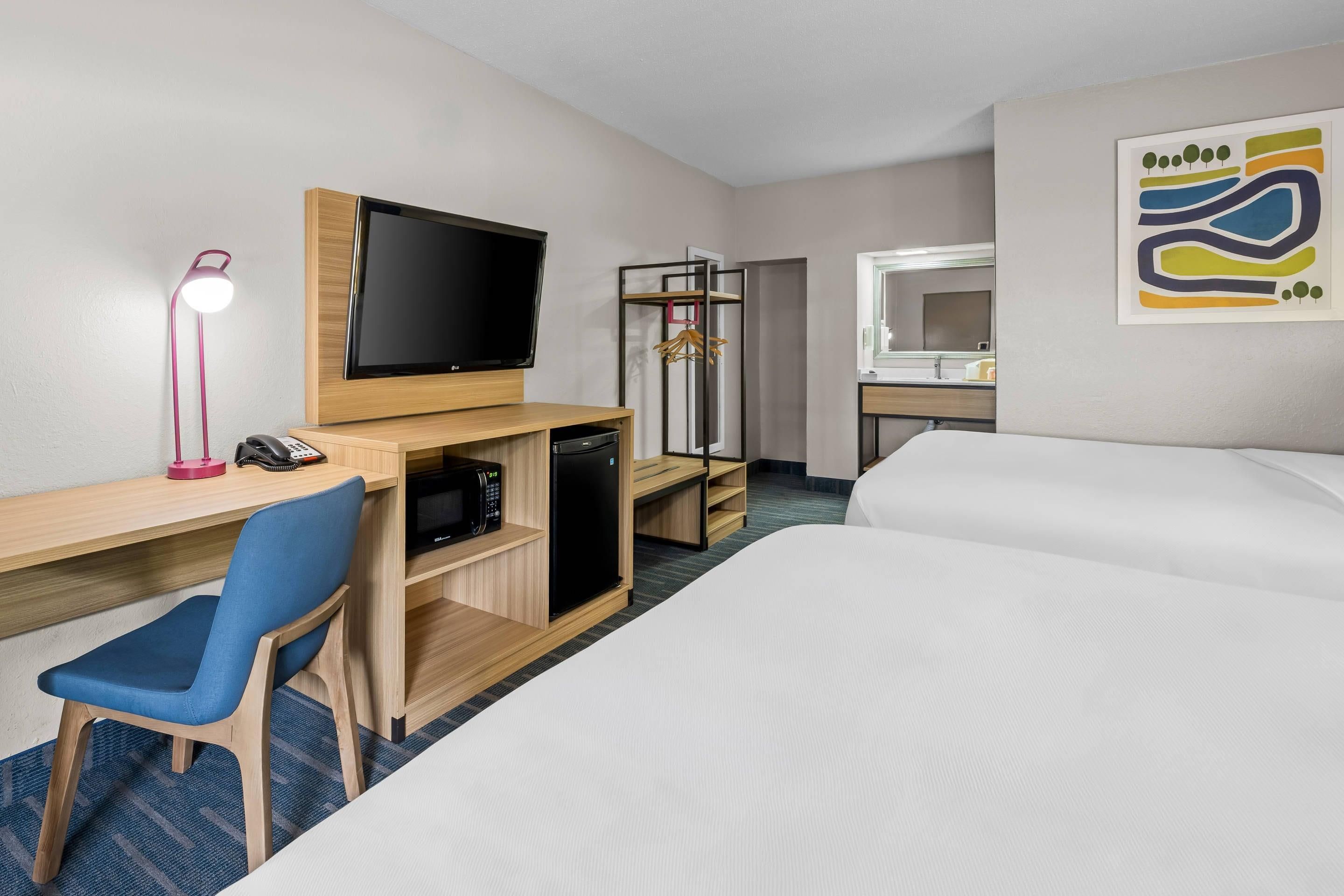 A hotel room with a bed, a desk with a computer, a TV, a microwave, and a mirror.