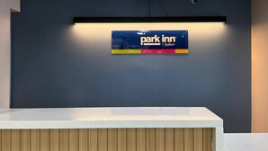 A reception desk with a sign for 'Park Inn by Radisson' and a security camera above it. - Park Inn by Radisson, Weldon - Roanoke Rapids (Weldon)