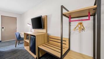 Ein Hotelzimmer mit einem Etagenbett, einem Schreibtisch, einem Flachbildfernseher, einem Stuhl und einem kleinen Kühlschrank.