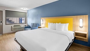 A hotel room with a large bed, a seating area with a chair, a built-in heater, and a window with a view of the outside. - Park Inn by Radisson, Weldon - Roanoke Rapids (Weldon)