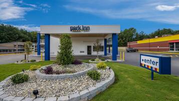 A park inn with a clear entrance, a landscaped garden, and a sign indicating the direction to the parking area.