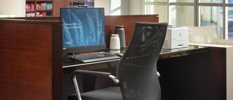 A hotel reception area with a computer desk, a chair, a printer, and a large window.