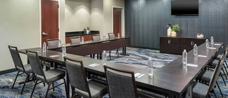 A conference room with a long table, chairs, a TV, and a small kitchenette.