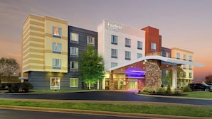 Ein mehrstöckiges Hotel Fairfield Inn & Suites mit modernem Design, das eine markante Fassade aus Stein und beleuchtete Beschilderung hat.
