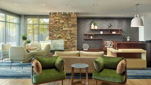 Ein modernes Wohnzimmer mit einer Wand aus Stein, einem Sofa, Sesseln, einem Couchtisch und einer Küchenzeile mit Regalen und einer Pendelleuchte.