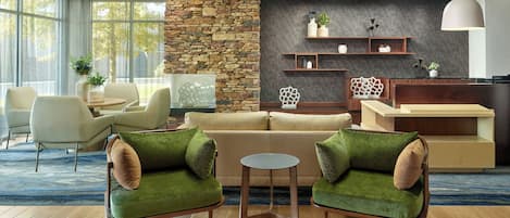 Uma sala de estar moderna com uma parede de destaque em pedra, um sofá, poltronas, uma mesa de centro e uma área de cozinha com prateleiras e uma luminária pendente.