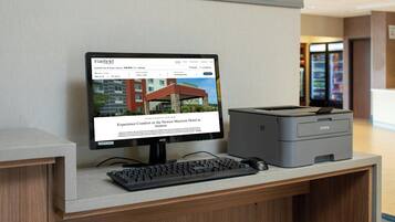 A hotel reception desk with a computer monitor displaying a booking page for Fairfield Inn & Suites Atmore, a keyboard, a mouse, and a printer.
