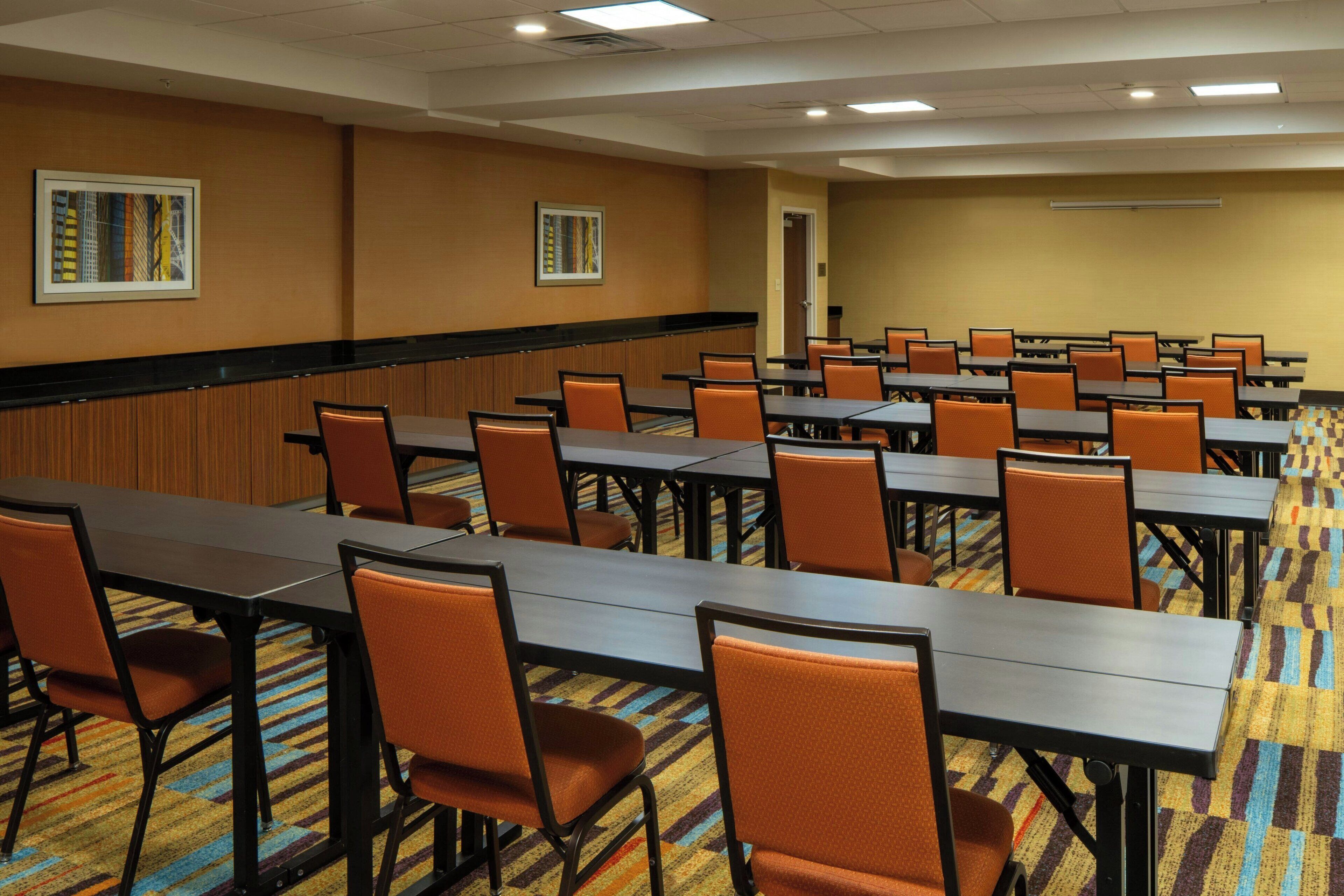 A conference room with multiple tables and chairs, a patterned carpet, and framed artwork on the walls.