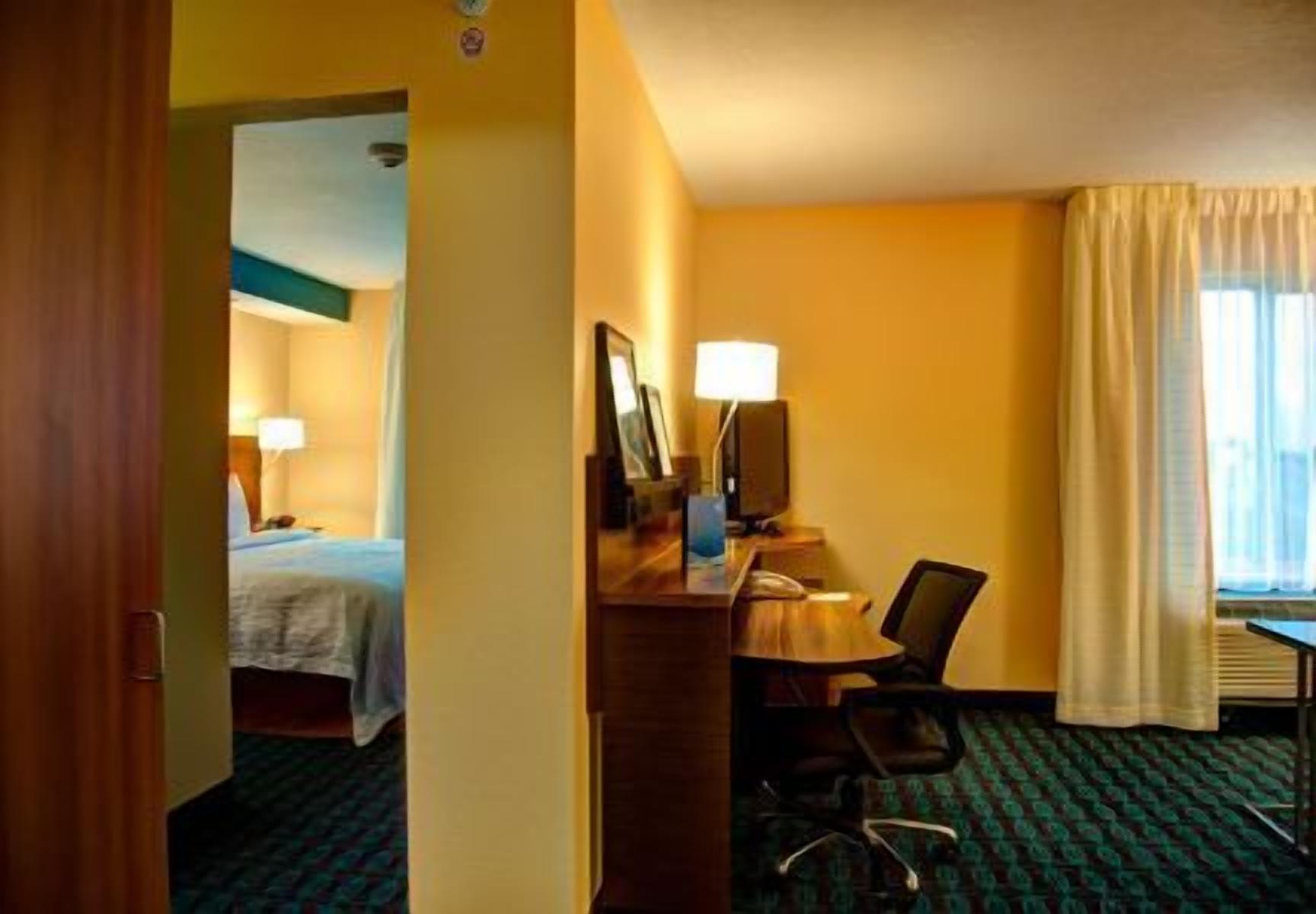 Een hotelkamer met een bed, een bureau met stoel, een lamp en een raam met gordijnen.