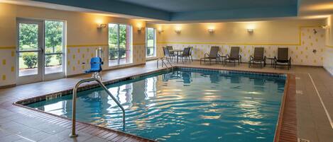An indoor swimming pool with a tiled floor, a pool ladder, and several chairs along the wall.