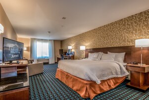 Habitación de hotel con una cama grande, un escritorio con computadora, televisión y ventana con cortinas.