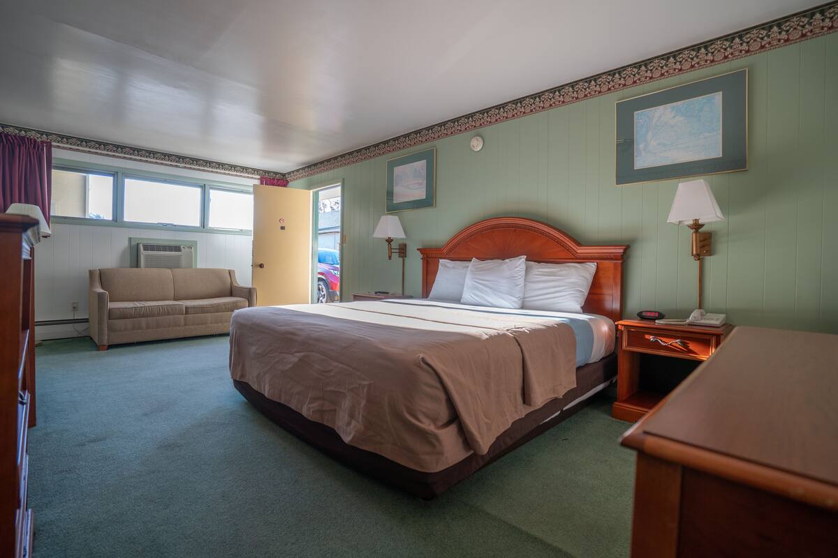 Una habitación de hotel con una cama grande, una mesita de noche de madera, una silla y una ventana.