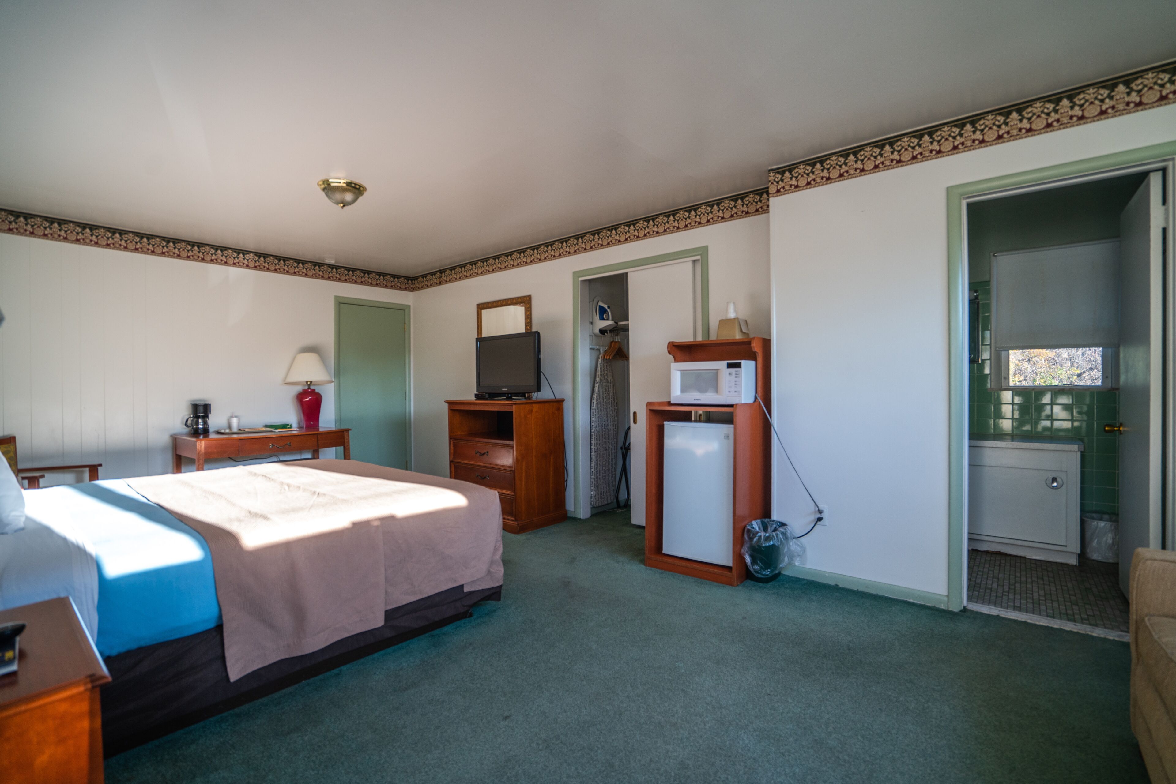 Una habitación de hotel con cama, escritorio, televisión, microondas y un refrigerador pequeño.
