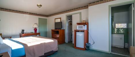 A hotel room with a bed, a desk, a television, a microwave, and a small refrigerator.