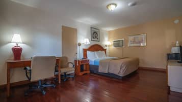 Hotelkamer met een houten bureau, stoel, nachtkastje, lamp, bed en een wandairconditioner.