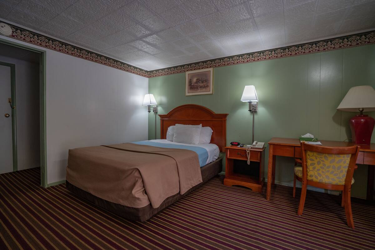 Una habitación de hotel con cama, lámparas de noche, un escritorio y una silla.
