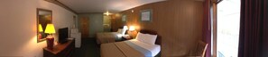 A hotel room with two beds, a desk with a lamp, a mirror, and a window with curtains.