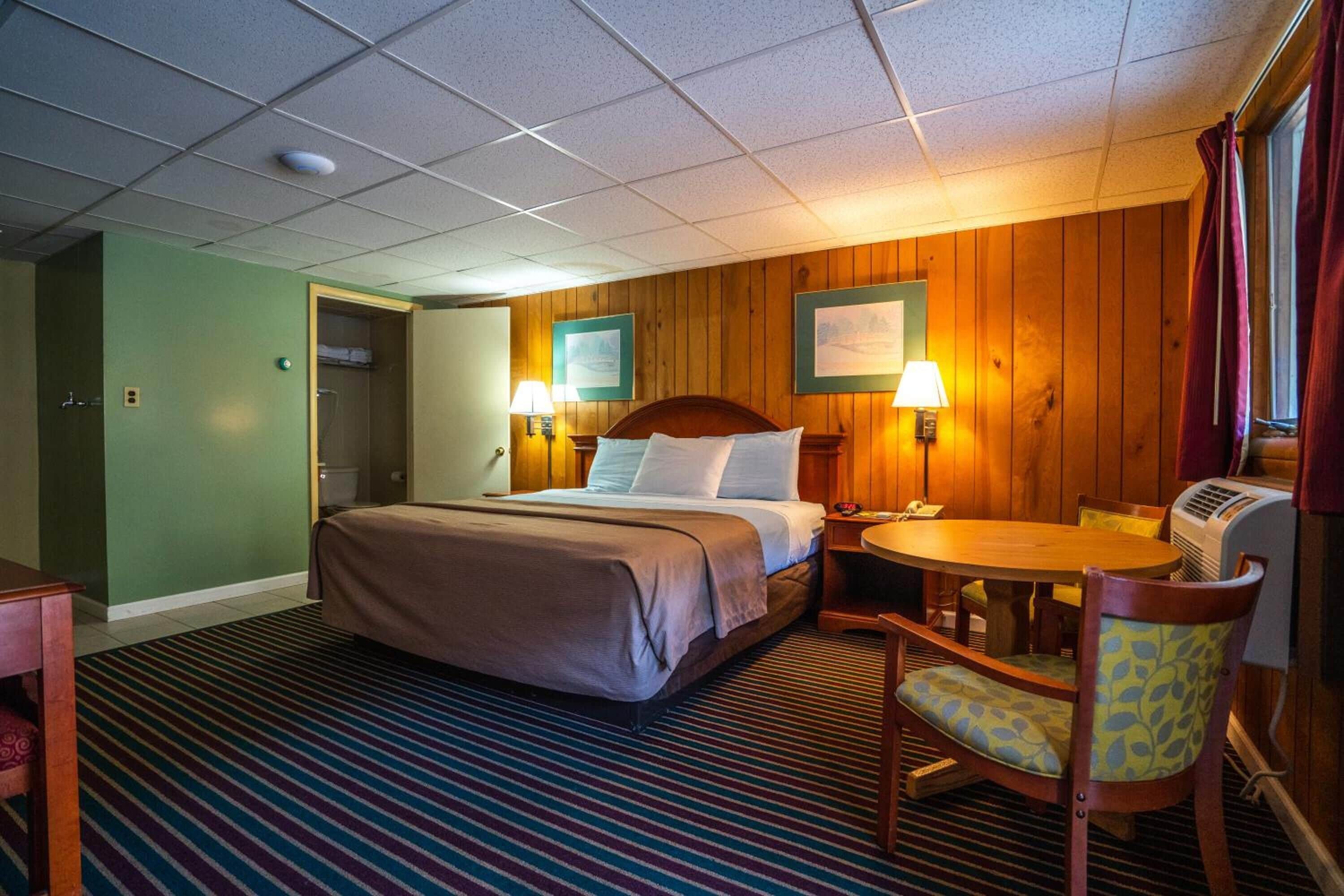 Una habitación de hotel con cama, lámparas de noche, una mesita y una silla.