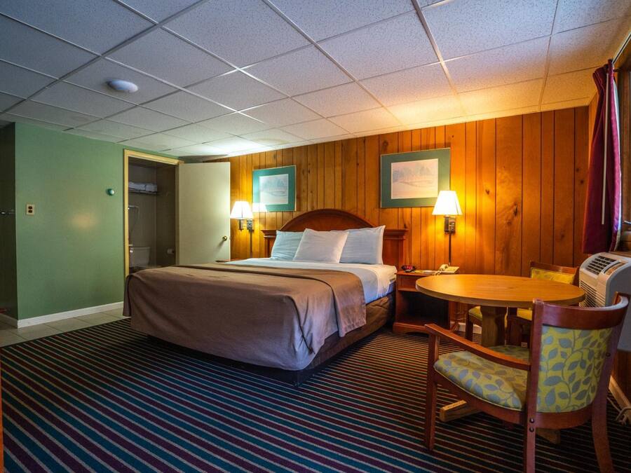 A hotel room with a bed, bedside lamps, a small table, and a chair.