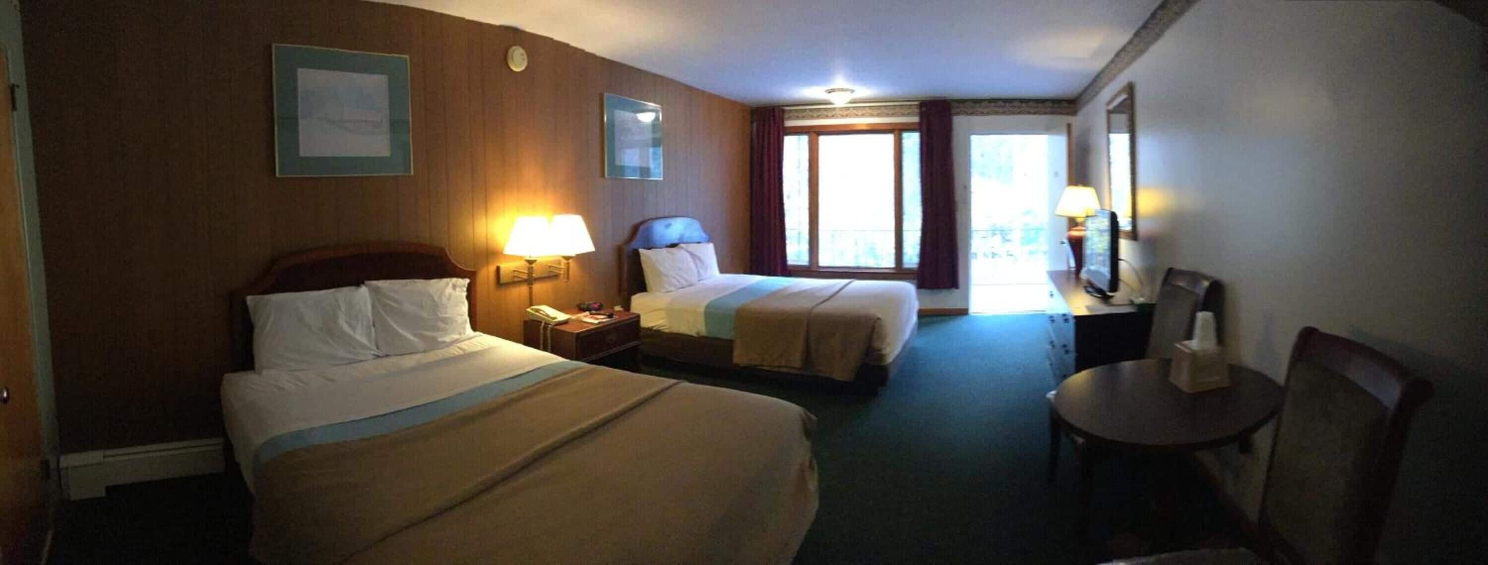 Ein Hotelzimmer mit zwei Betten, einem Schreibtisch, einem Stuhl, einem Nachttisch und einem Fenster mit Vorhängen.