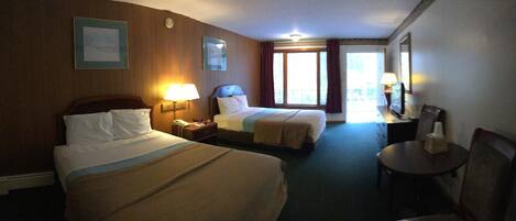 Habitación de hotel con dos camas, un escritorio, una silla, una mesita de noche y una ventana con cortinas.